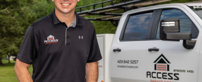 A man wearing an Access Garage Doors uniform and cap stands next to a branded company truck parked outdoors on a driveway.